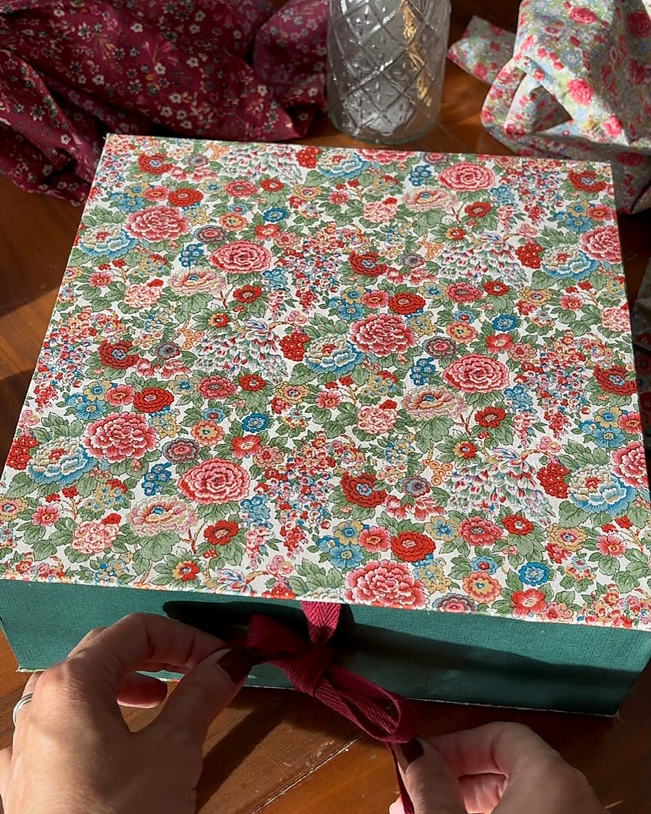 Manos anudando el lazo burdeos de la caja de regalo del kit de Manzanas Liberty