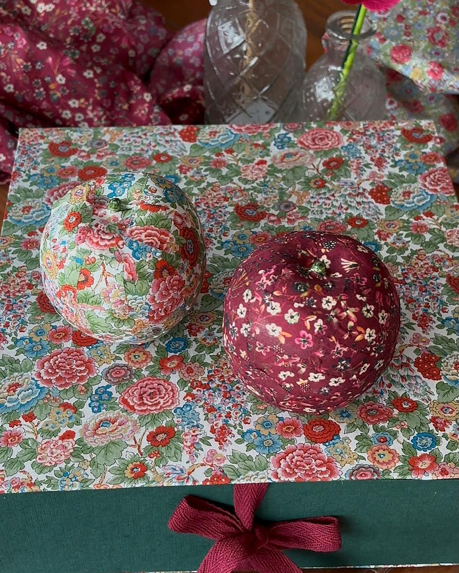 Dos manzanas navideñas terminadas descansan sobre la caja de regalo de tela Liberty