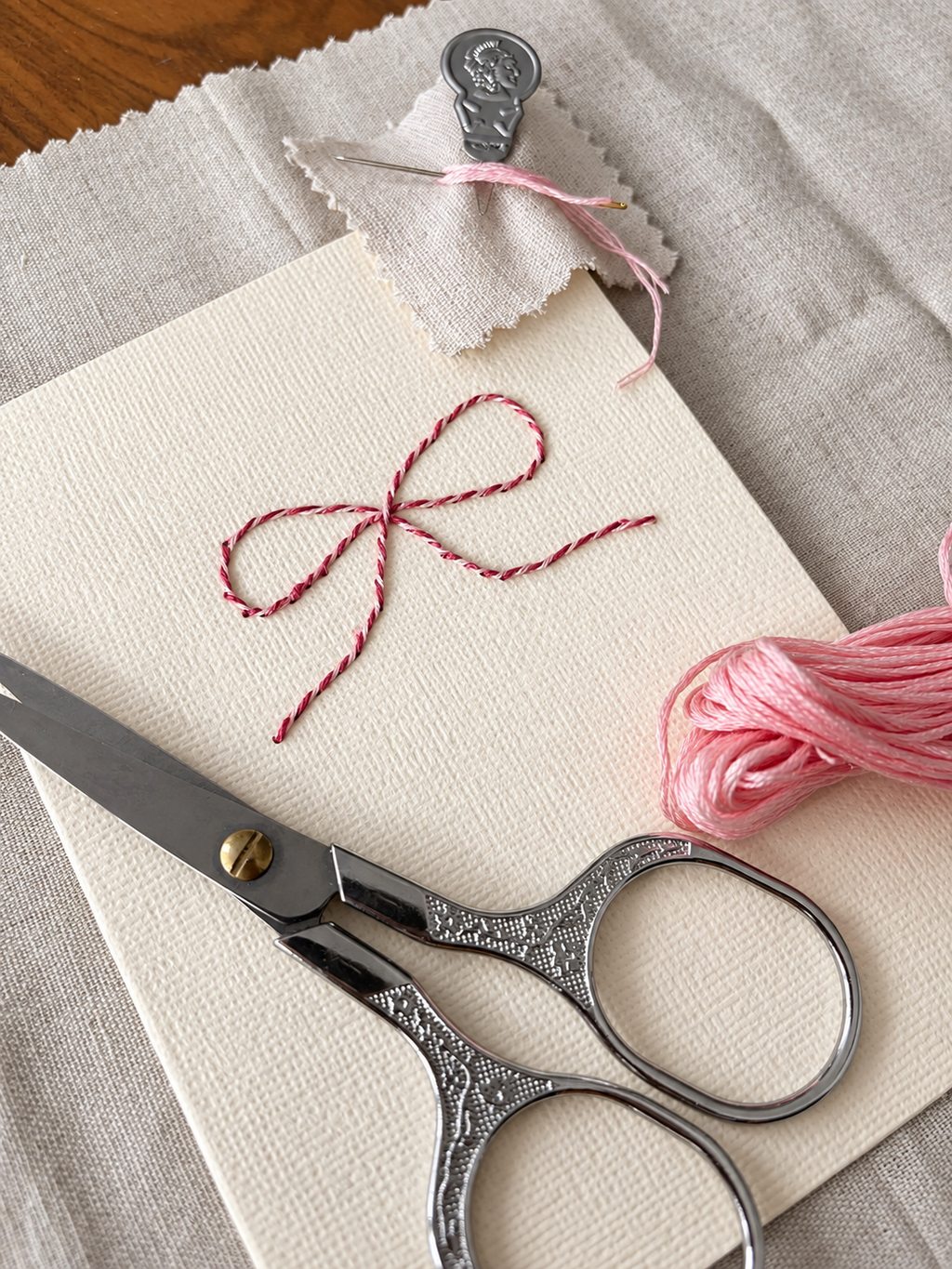 Detalle en perspectiva de un lazo rosa y granate bordado sobre una tarjeta, con hilo y tijeras del kit Slow Mail Atelier de Mery’s Moment.